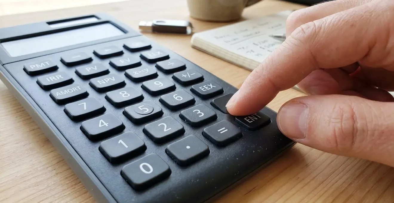 Gros plan sur une main posée sur une calculatrice financière moderne, touches de fonction visibles, arrière-plan flouté avec documents de bureau